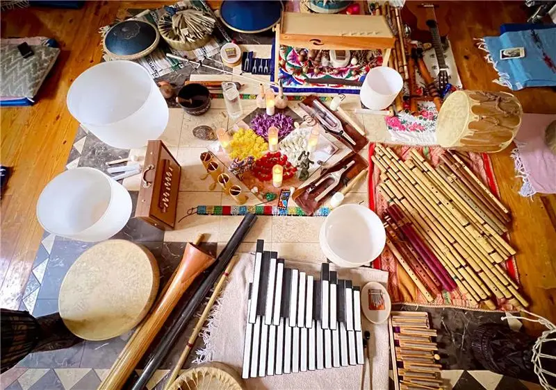 An overhead view of a diverse collection of sound healing instruments, including crystal singing bowls, flutes, and percussion, set up for a therapeutic session at Sage Holistic Arts.